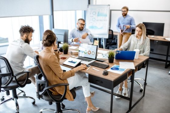 Group of diverse colleagues working in the modern office, having discussion or small conference on a working place with computers being cooled by a portable spot cooler in Newark