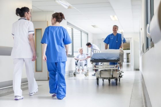 Male nurse pushing stretcher gurney bed in hospital corridor with doctors & senior female